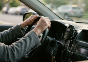 Close-up view of a car dashboard with ignition interlock device mounted, early morning light coming through windshield, driver’s hands resting on steering wheel in a moment of frustration, keys in ignition